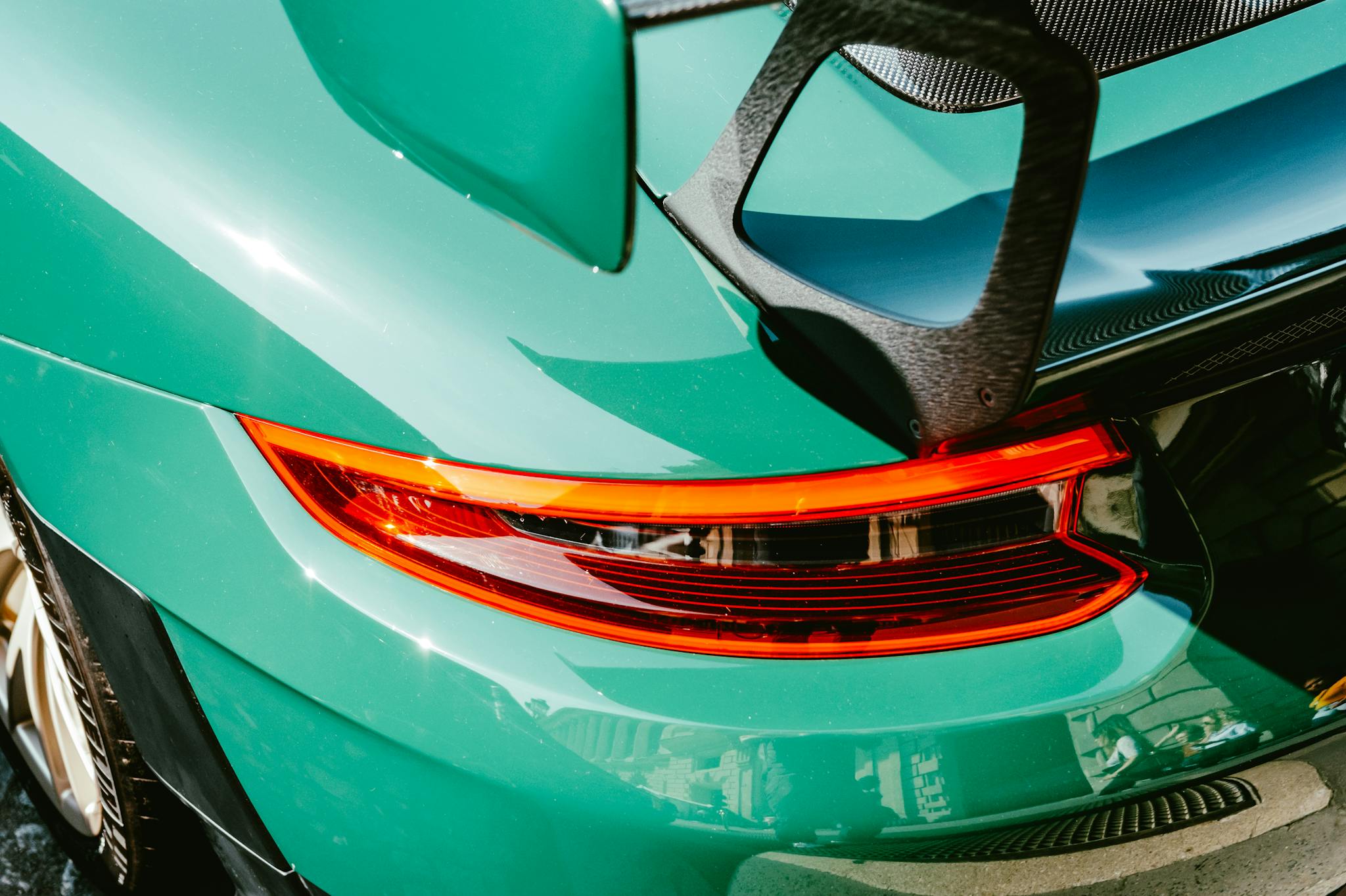 Close-up of a glossy green sports car featuring a rear spoiler and tail light reflection.