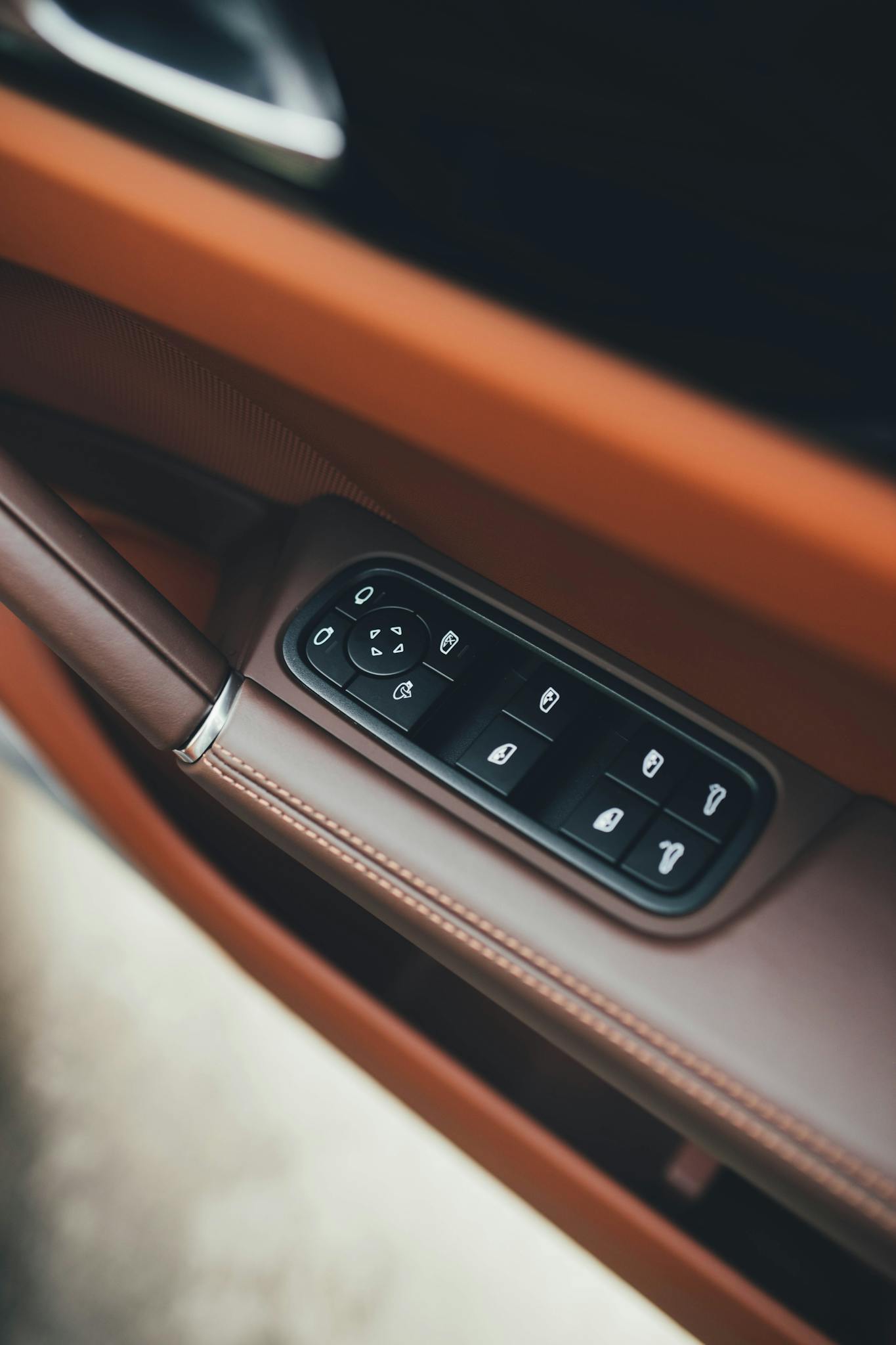 Close-up of a luxury car interior showing brown leather and control buttons on the door panel.